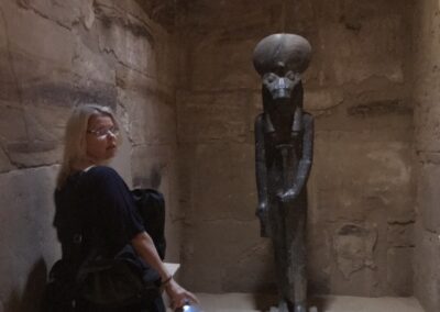 Girl facing black granite lioness statue of Sekhmet in shrine turns head to camera