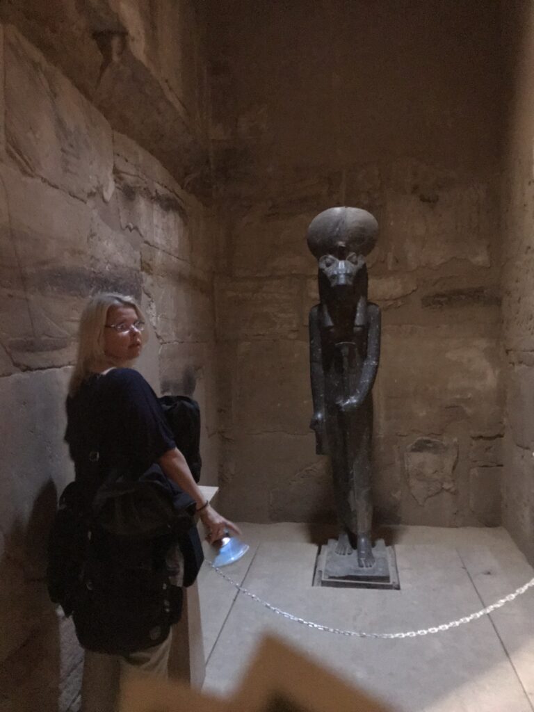 Girl facing black granite lioness statue of Sekhmet in shrine turns head to camera